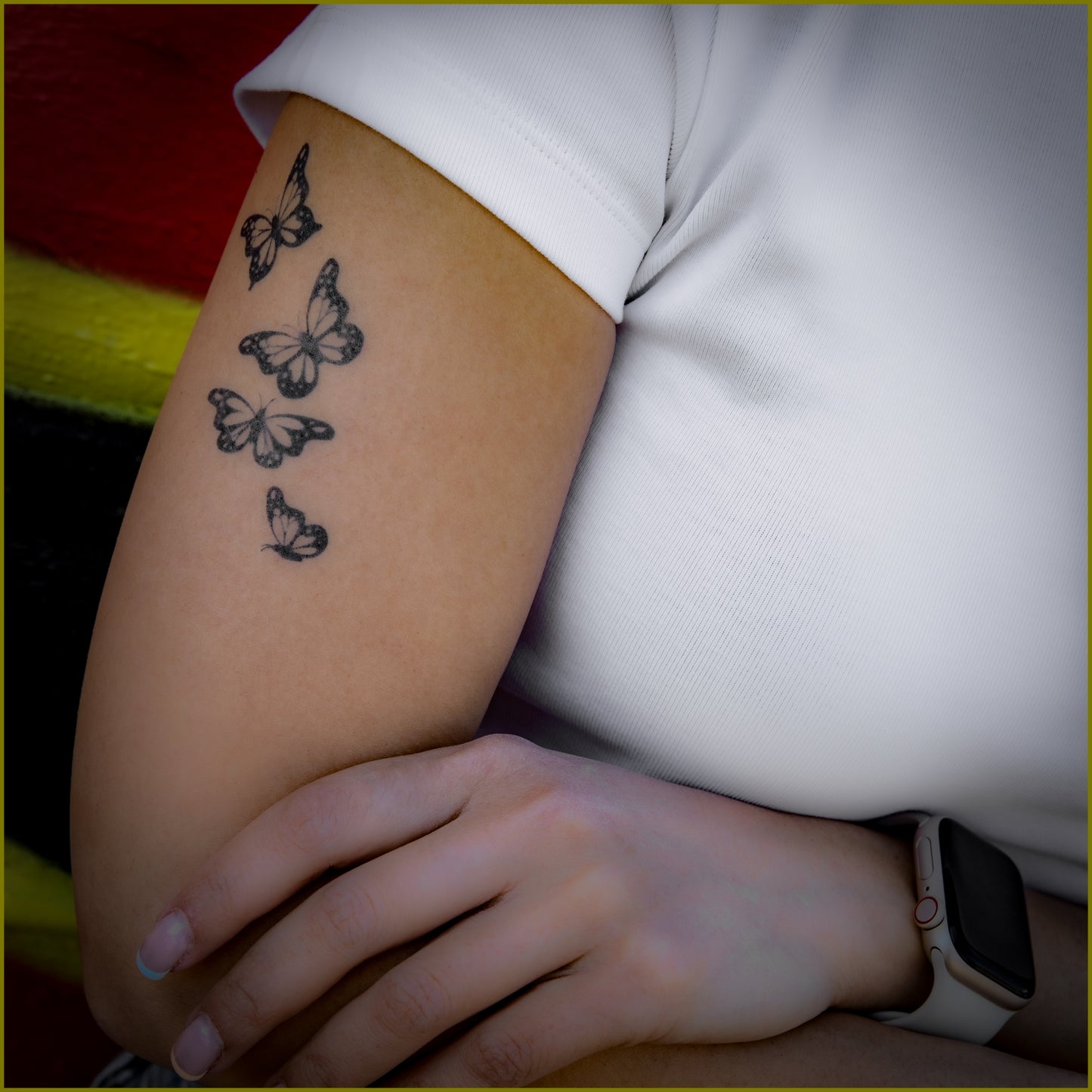 A woman is resting her left hand on her right forearm. There is a tattoo of 4 butterflies on her right upper arm.